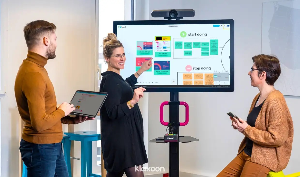 Trois personnes autour d’un MeetingBoard affichant un Board d’idées et plusieurs fichiers PowerPoint
