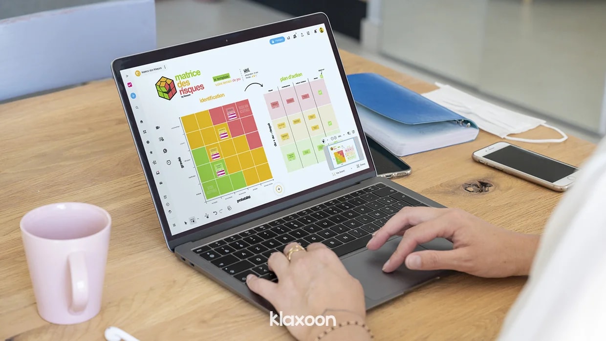 Une personne travaillant sur un ordinateur qui affiche un Board avec le template de la méthode Matrice des risques. | Klaxoon