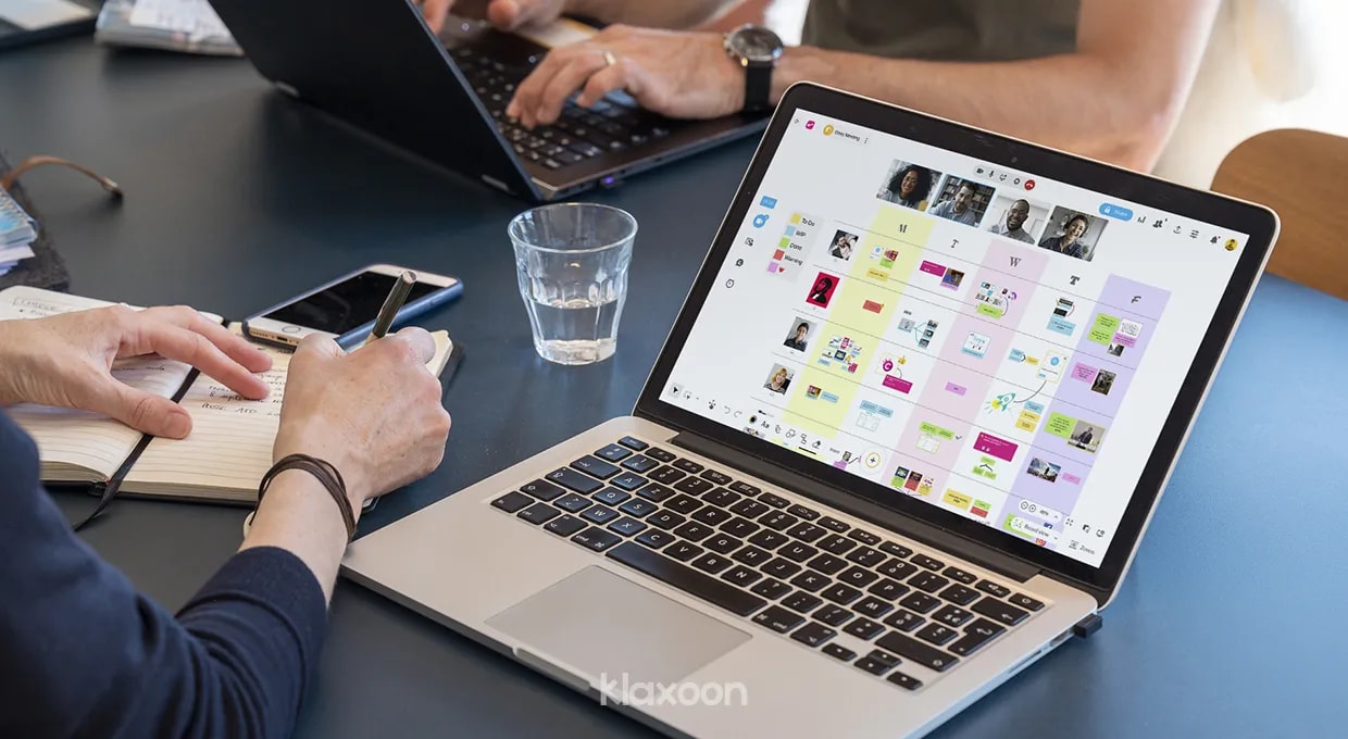 Une personne travaillant sur un carnet et sur un ordinateur qui affiche un modèle de whiteboard de réunion hebdomadaire. | Klaxoon