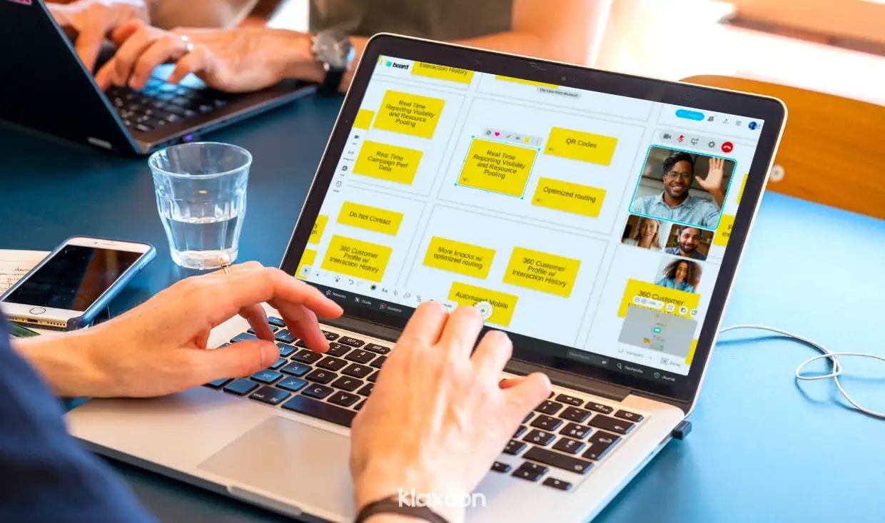 A person working on a computer displays a Board with several ideas, some of which are liked by participants connected by video. | Klaxoon