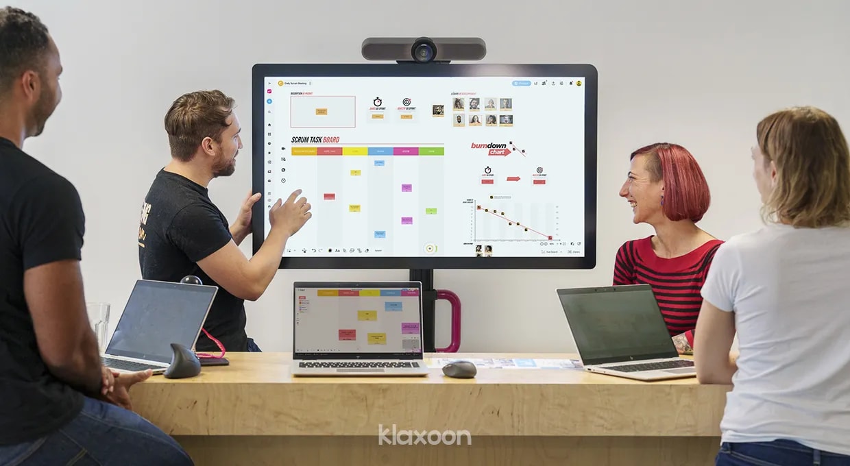 Four people gathered around a large screen displaying an interactive whiteboard. | Klaxoon