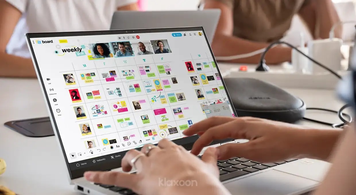 A person working on a computer displaying a Klaxoon Board where several people have shared their ideas in a structured way at a table. | Klaxoon
