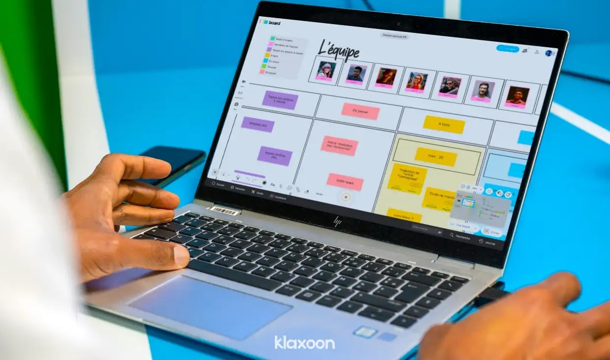 Une personne travaillant sur un ordinateur où s’affiche un Board avec des photos des membres de l’équipe et des idées catégorisées par code couleur. | Klaxoon