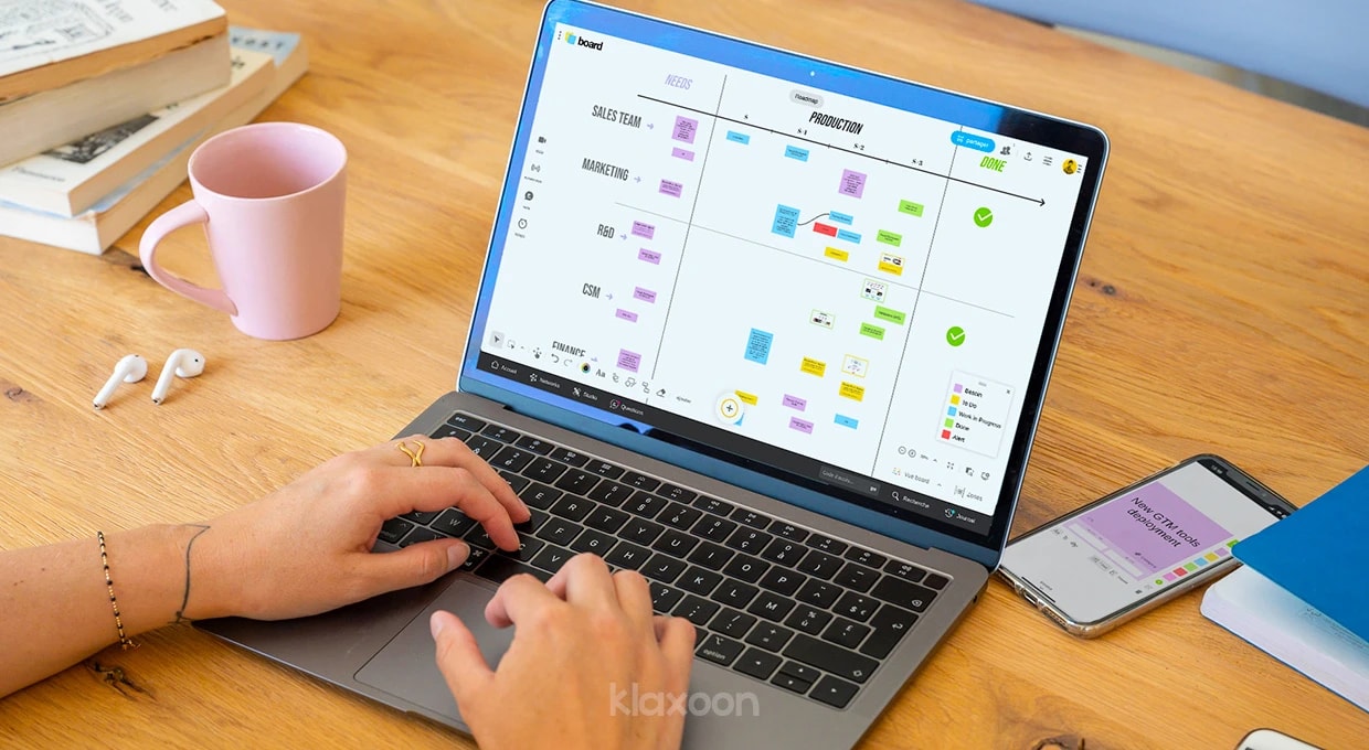 Une personne travaillant sur un ordinateur où s’affiche un Board avec un planning de déploiement de la plateforme sur plusieurs équipes. | Klaxoon