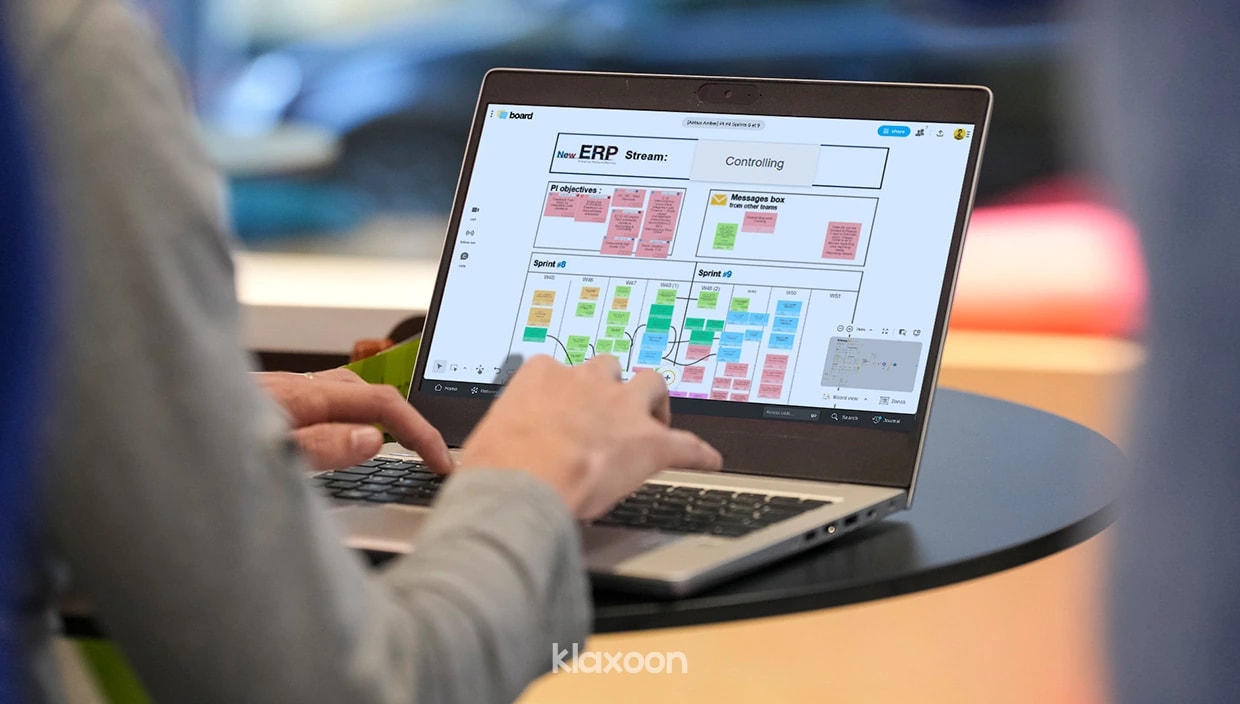 Une personne qui travaille sur un ordinateur affichant un Board rempli par l’équipe, et structuré d’après le template PI Planning de Klaxoon. | Klaxoon