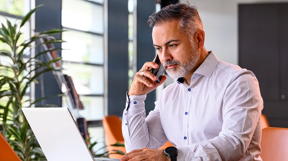 Une personne travaillant devant un ordinateur et écoutant son téléphone. | Klaxoon