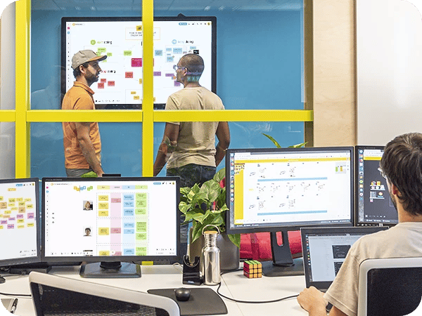 Desktop monitor showing Wrike work management platform with task list and timeline view.