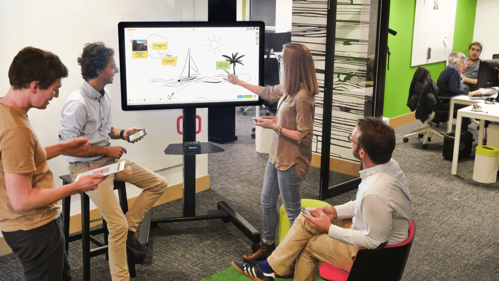 Four people gathered around a big screen displaying the Speed Boat template. | Klaxoon