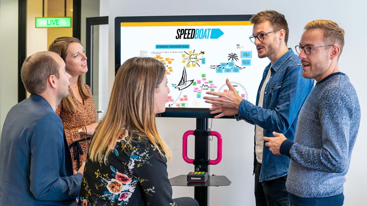 Un groupe de 5 personnes réuni autour d'un grand écran qui affiche une rétrospective Speed Boat. | Klaxoon