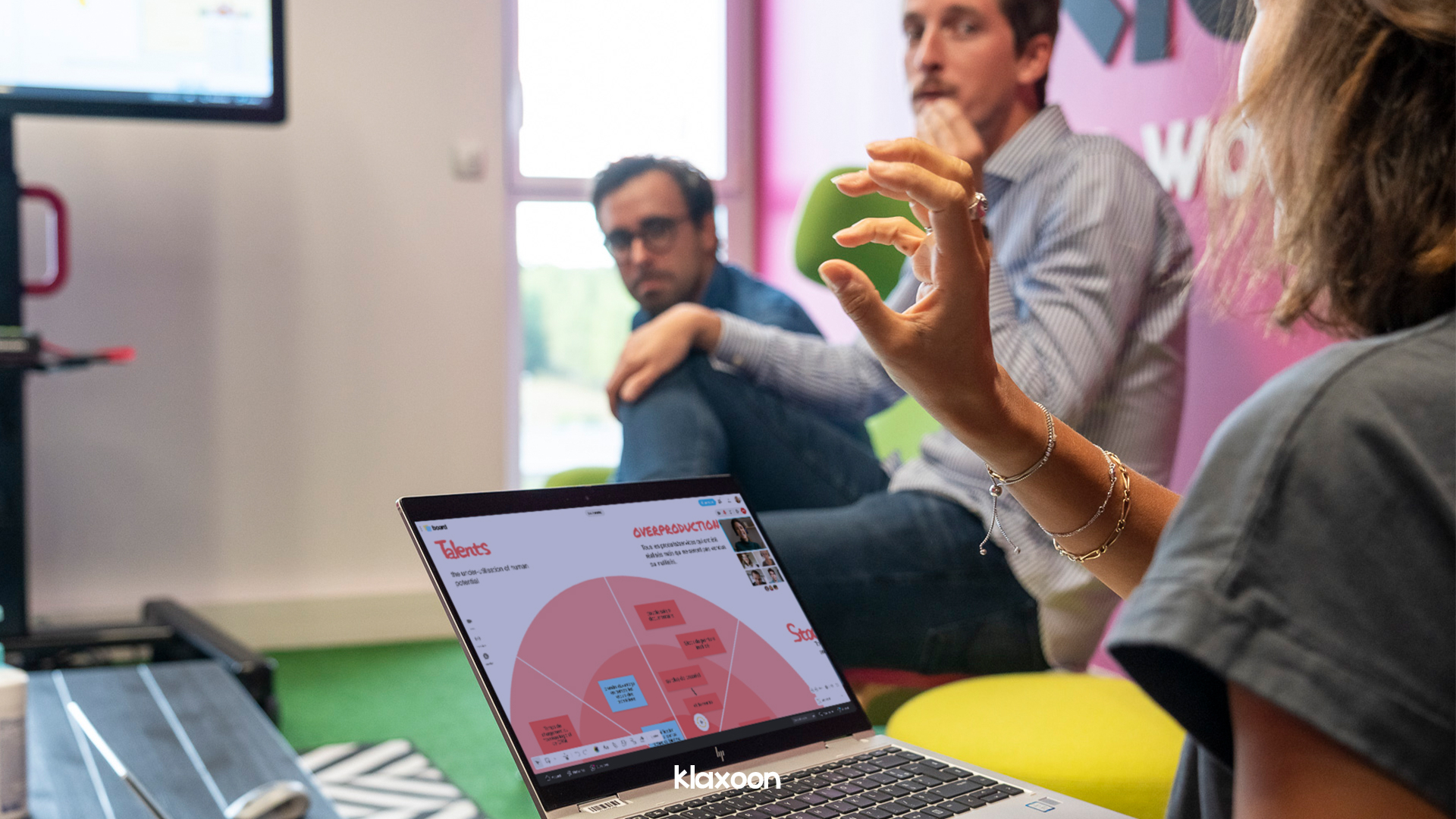 A team of 3 people in a room working on a "8 Wastes of Lean" template, with other people connected through videoconference. | Klaxoon