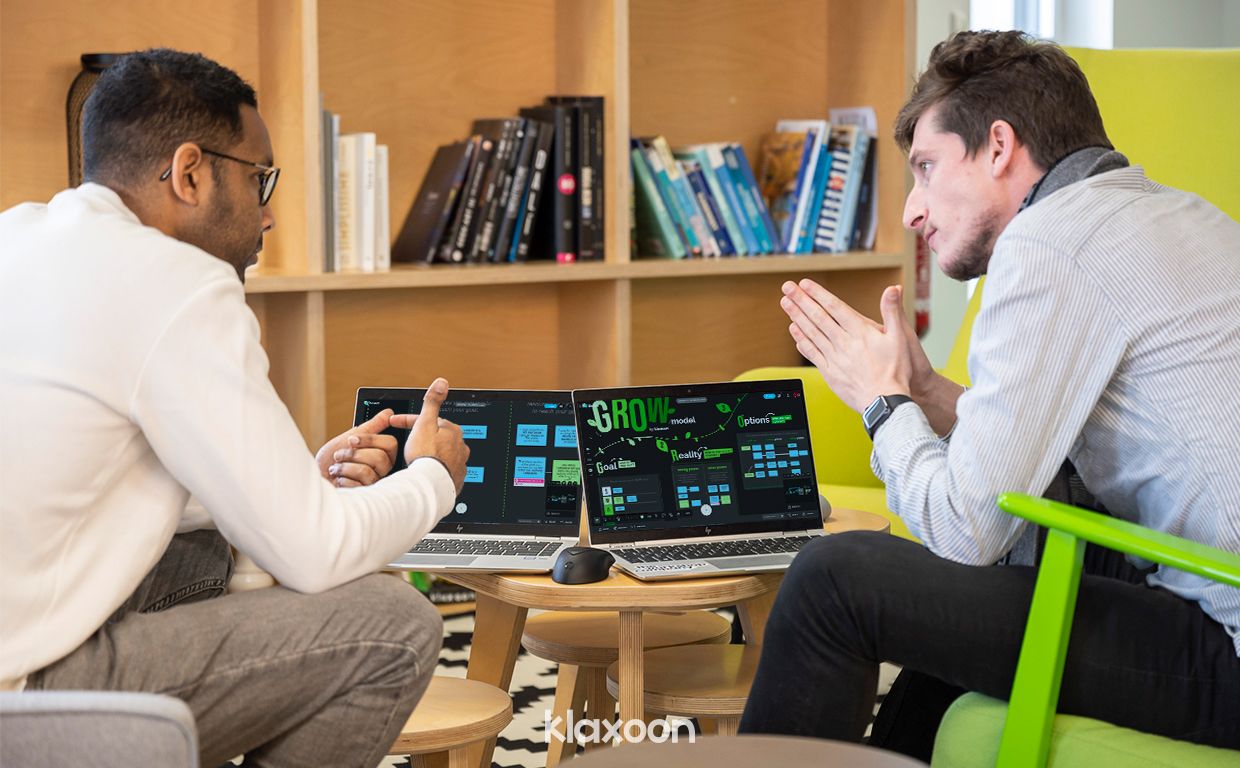 Deux personnes assises dans des fauteuils qui discutent, avec des ordinateurs portables posés devant elles. | Klaxoon