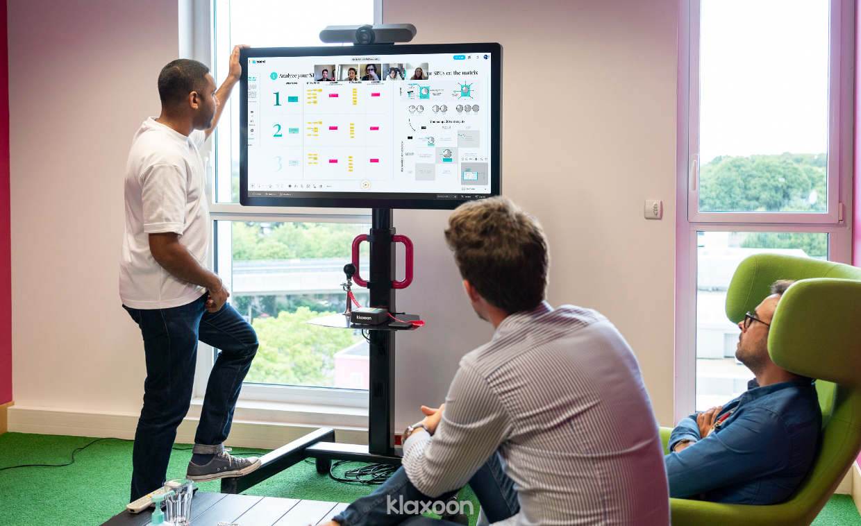 Three people are gathered around a screen on which Board allows them to work with their remote co-workers. Together, they fill out the GE-McKinsey Matrix using the ready-to-use template. | Klaxoon