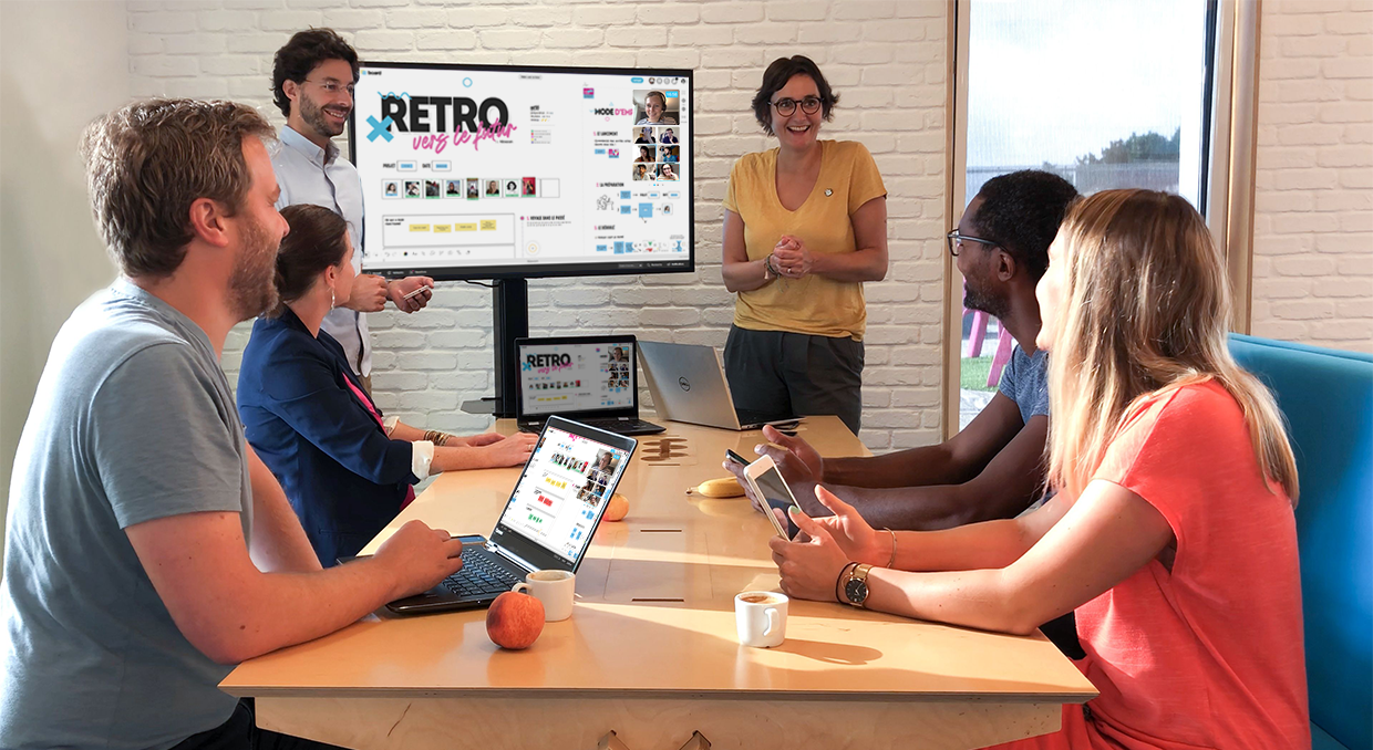 Une équipe de 6 personnes sur place et 7 personnes à distance en visio travaille sur le template Rétro dans le Futur à travers plusieurs écrans. | Klaxoon