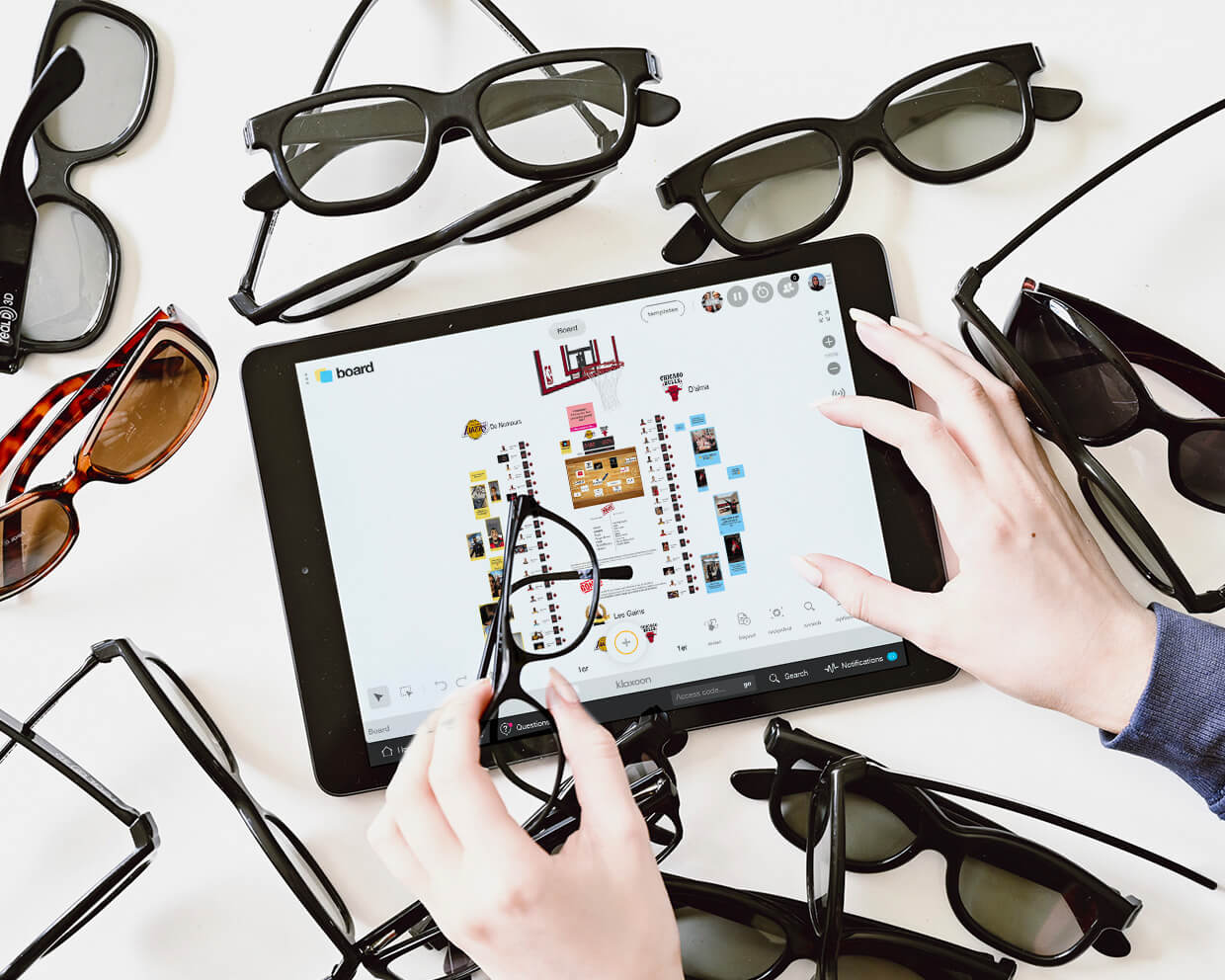 A tablet showing a Klaxoon Bord with a team challenge, surrounded by pairs of glasses. | Klaxoon
