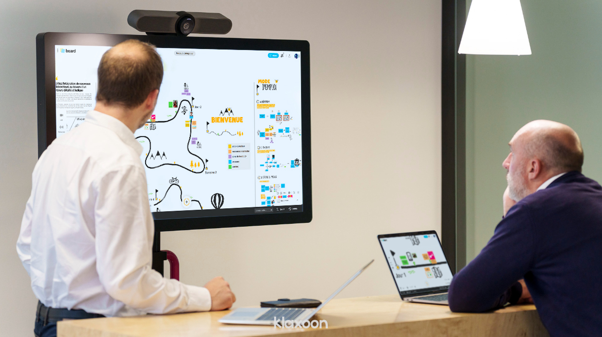 Deux personnes en présentiel travaillant sur plusieurs écrans de taille différente sur le template Onboarding sur Board. | Klaxoon
