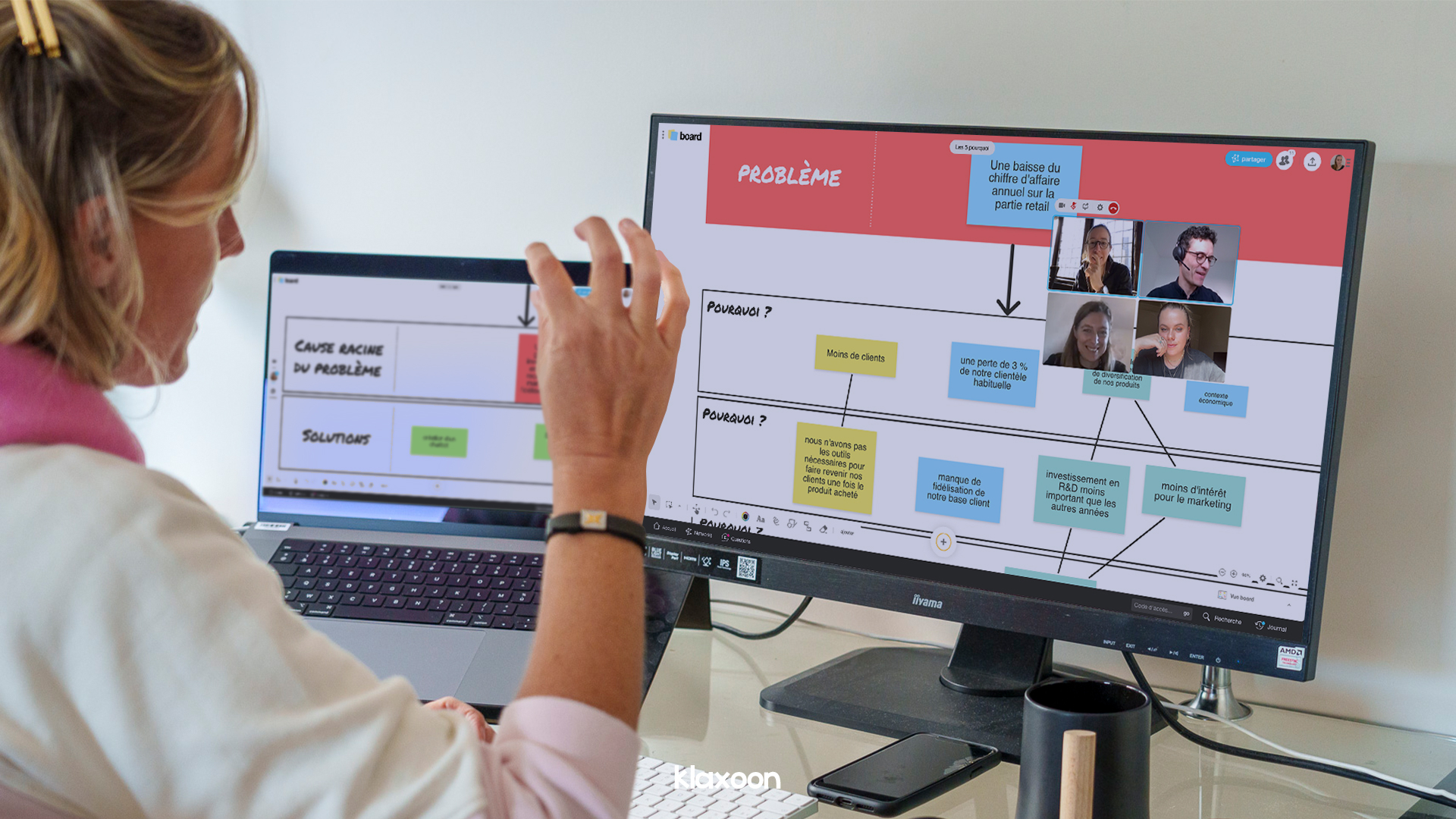 Une personne en réunion à distance avec son équipe visible en visio, utilisant le template des 5 pourquoi sur 2 écrans d'ordinateur. | Klaxoon